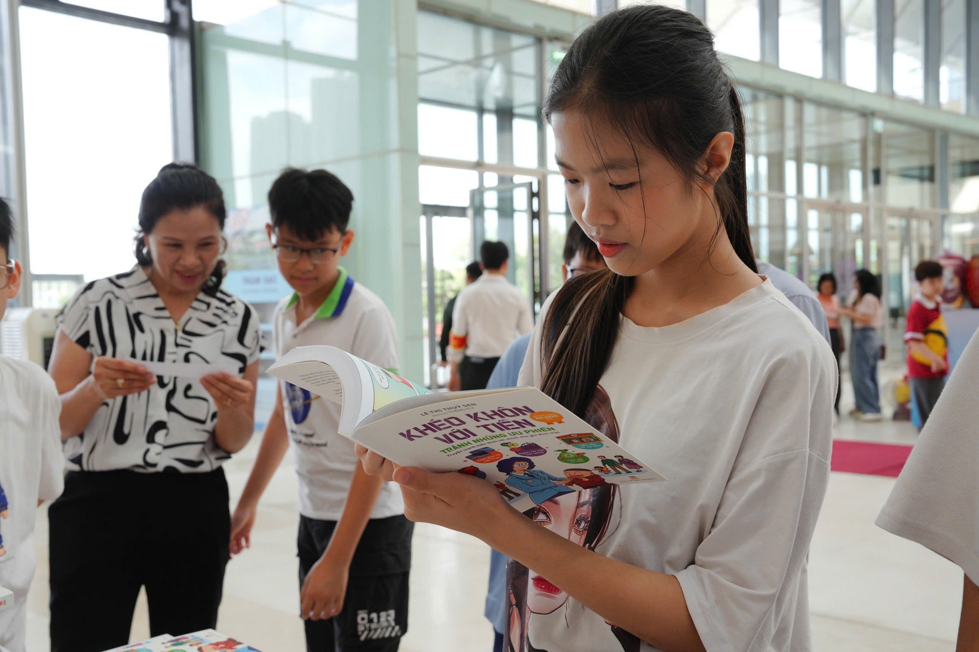 Một em nhỏ ngồi đọc say mê giữa dòng người tham quan